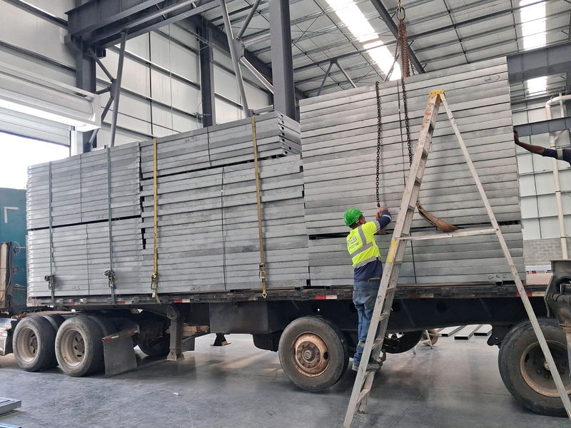 Operator guiding the crane loading of light-gauge steel panel bundles onto a flatbed inside the plant