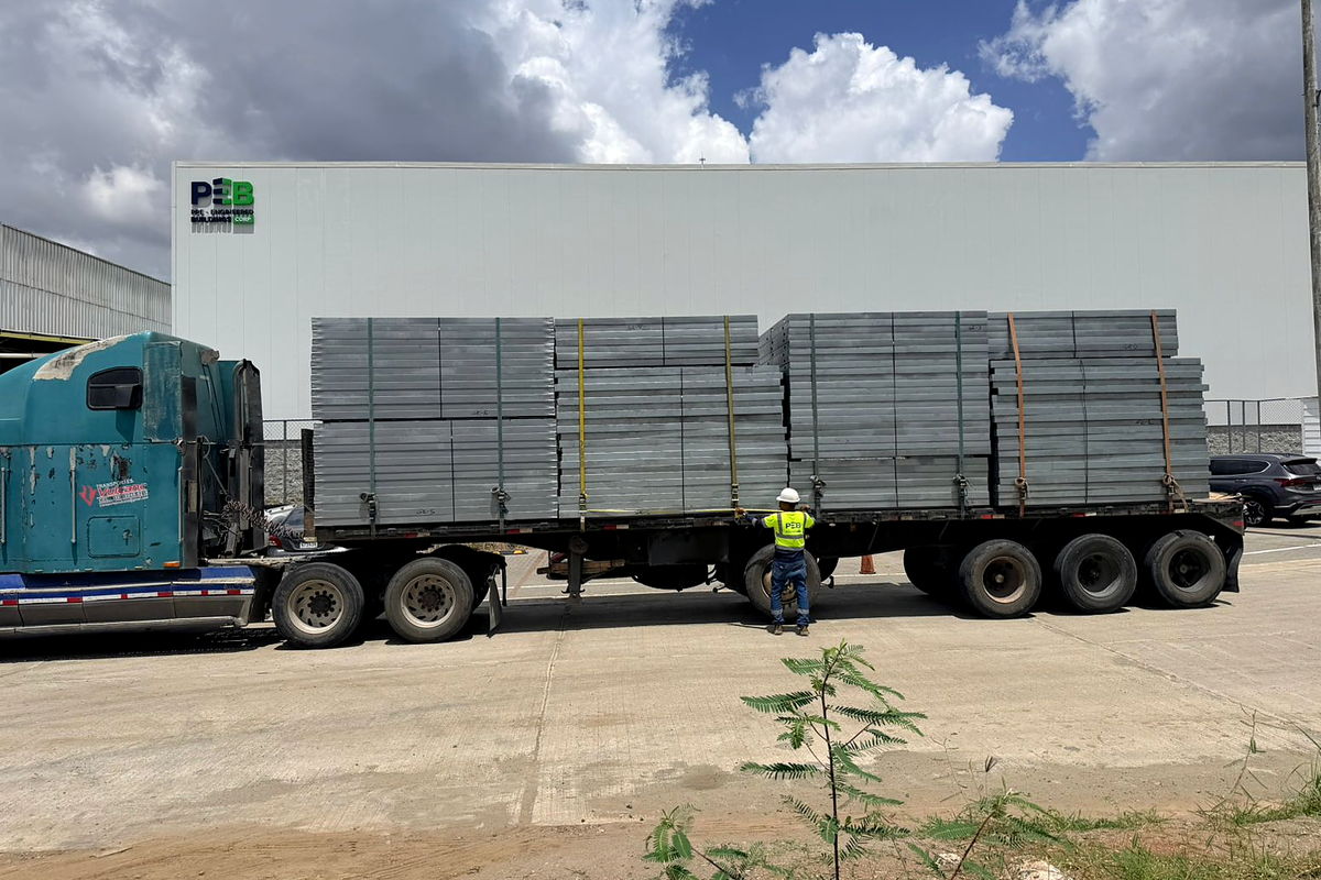 Flatbed truck loaded and strapped with light-gauge steel structural panels, ready to leave the NewCon Steel plant in Panama