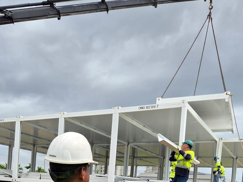 Crane lift of a light-gauge steel structural module during on-site erection, over concrete pedestals