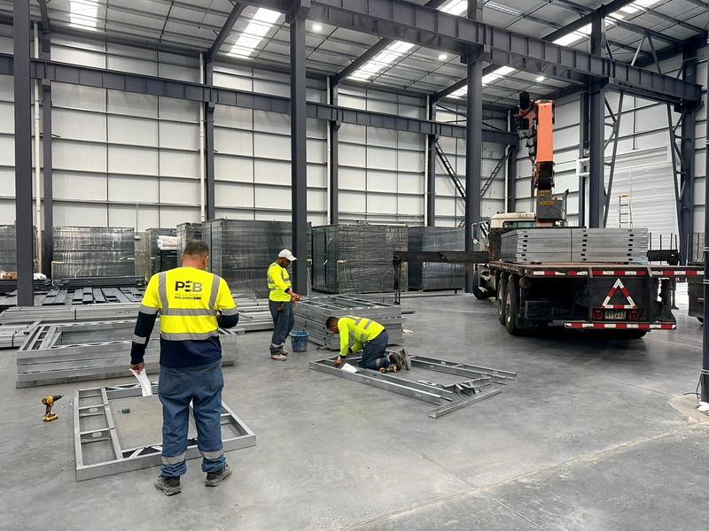 Operators screw-fixing light-gauge steel structural frames on the plant floor next to the profile stacks