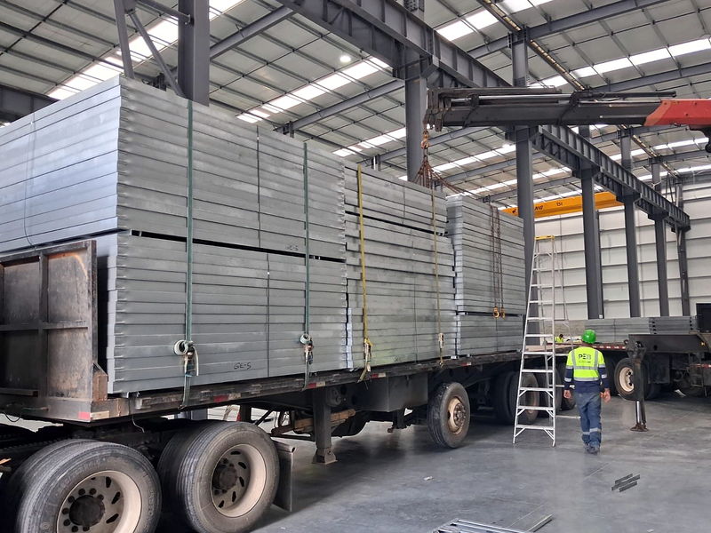 Bundles of light-gauge steel structural panels strapped on a flatbed and identified by batch inside the hall