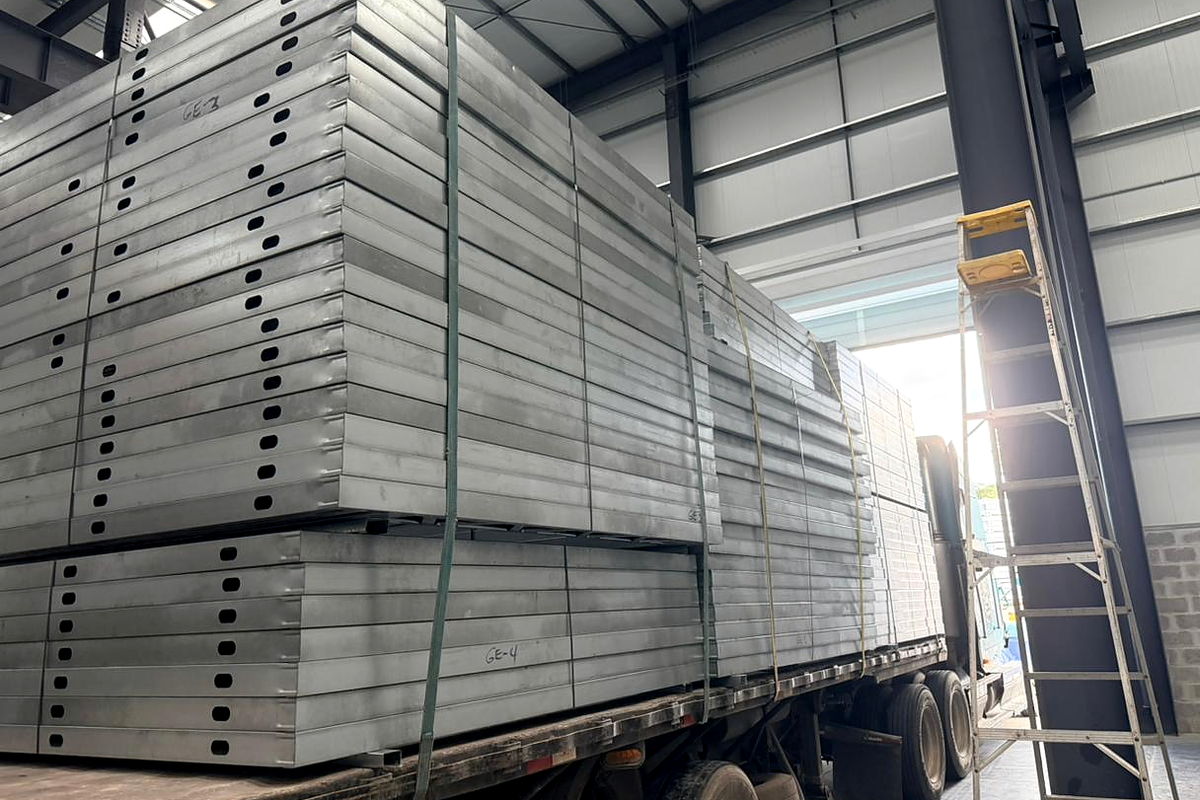Pre-assembled light-gauge steel structural panels with service punch-outs, stacked on a flatbed inside the plant