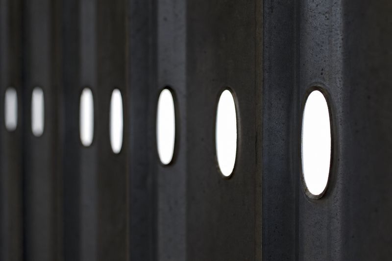 Oval service-hole punchings in a row of cold-formed steel studs, backlit